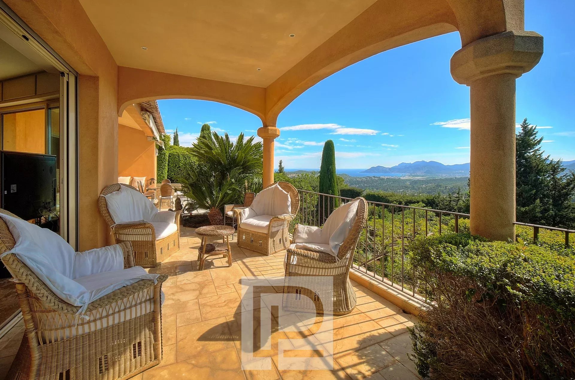 Une terrasse couverte avec des fauteuils en osier offre une vue panoramique sur un paysage montagneux et verdoyant.