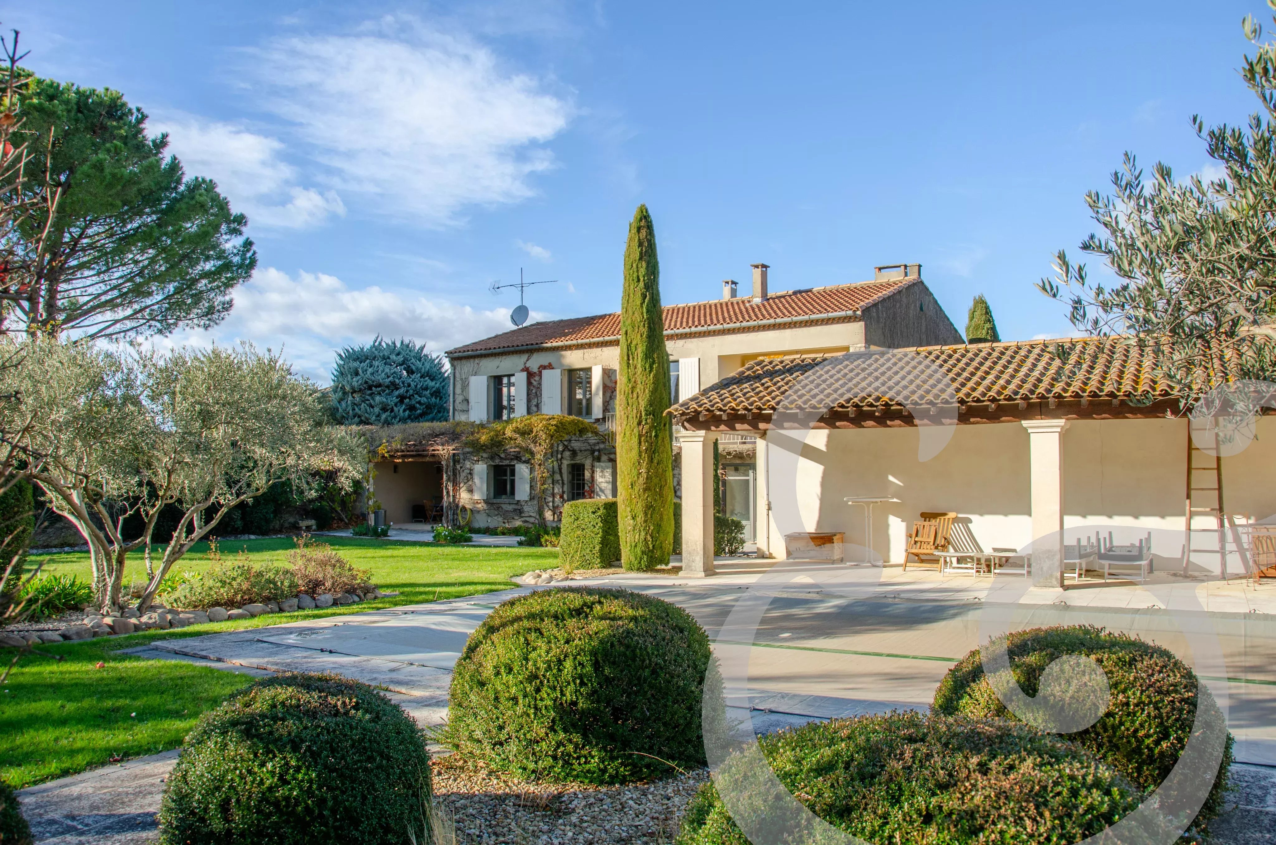 Grande piscine, pool house avec jardin bien entretenu et ciel bleu en arrière-plan.