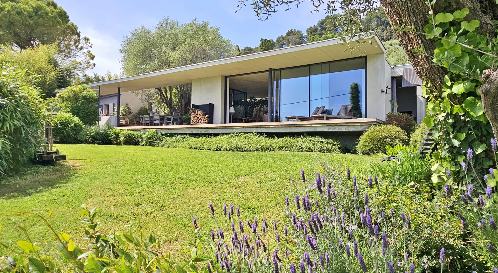 Villa Contemporaine entourée de verdure avec de grandes fenêtres et un jardin fleuri.