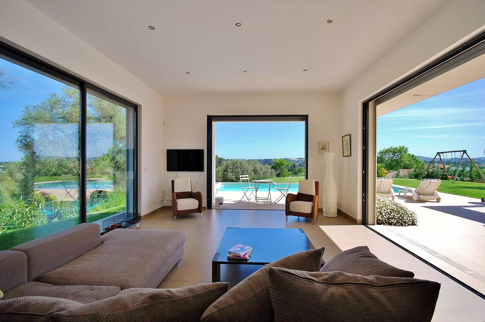 Une villa contemporaine avec des murs blancs, entourée de verdure, avec une piscine et des chaises longues sur une pelouse bien entretenue.