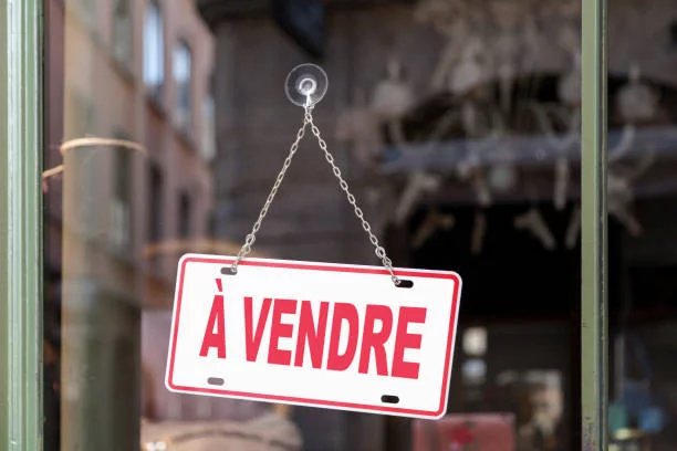 Close-up on a red sign in a window with written in it in French "? vendre", meaning in English "For sale".