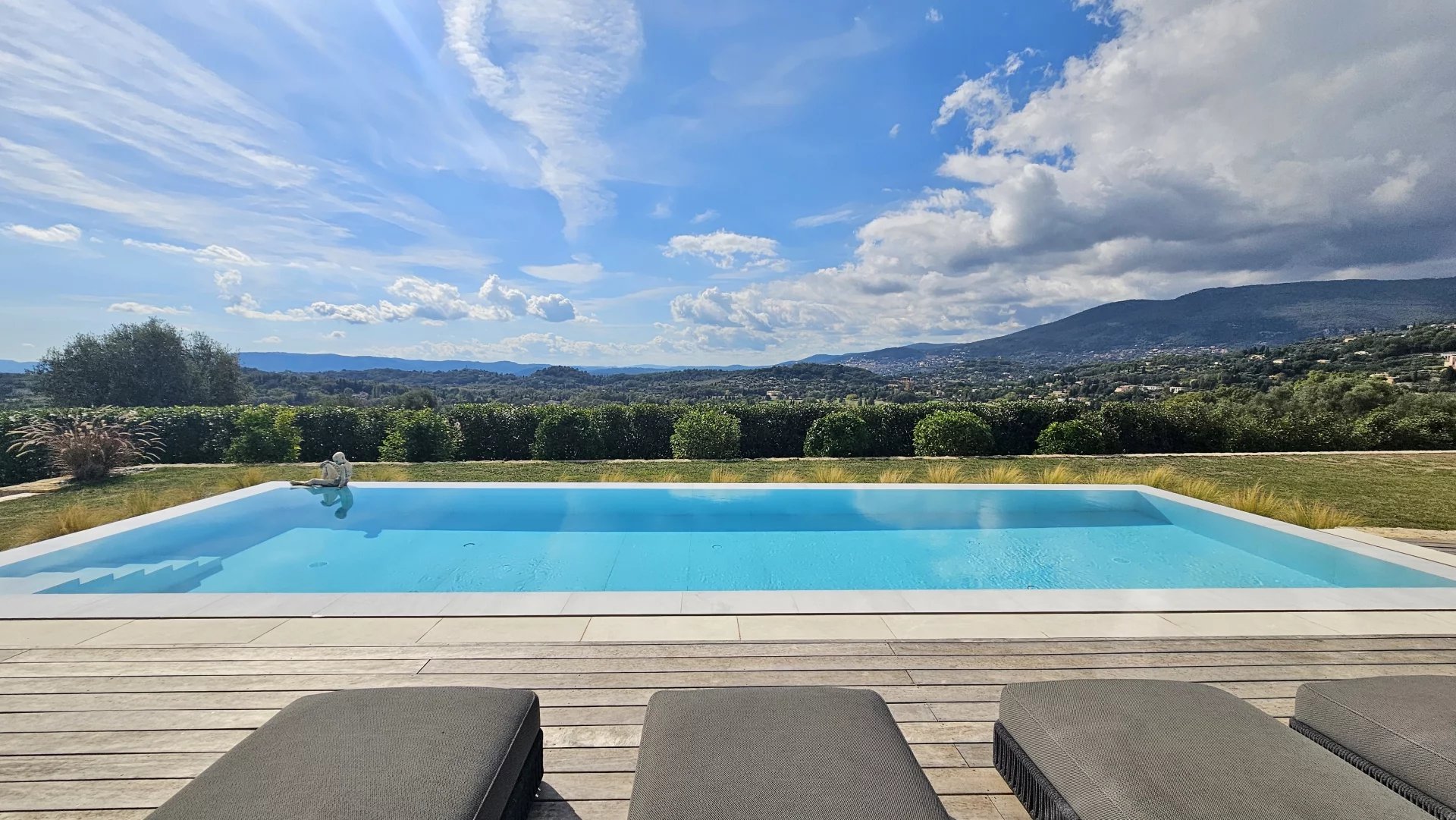 Belle maison moderne avec piscine, entourée de verdure, sous un ciel ensoleillé.