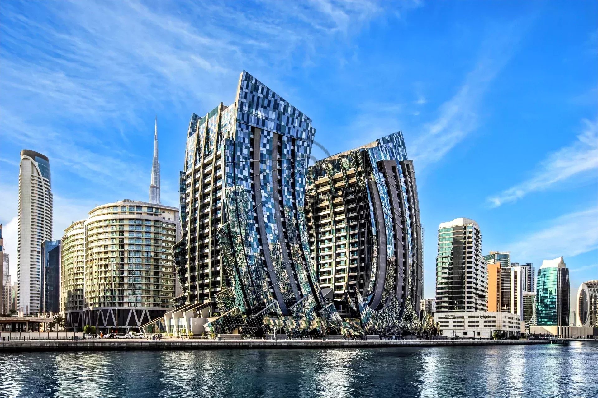 Edificios modernos y curvados junto a un canal bajo un cielo azul claro.