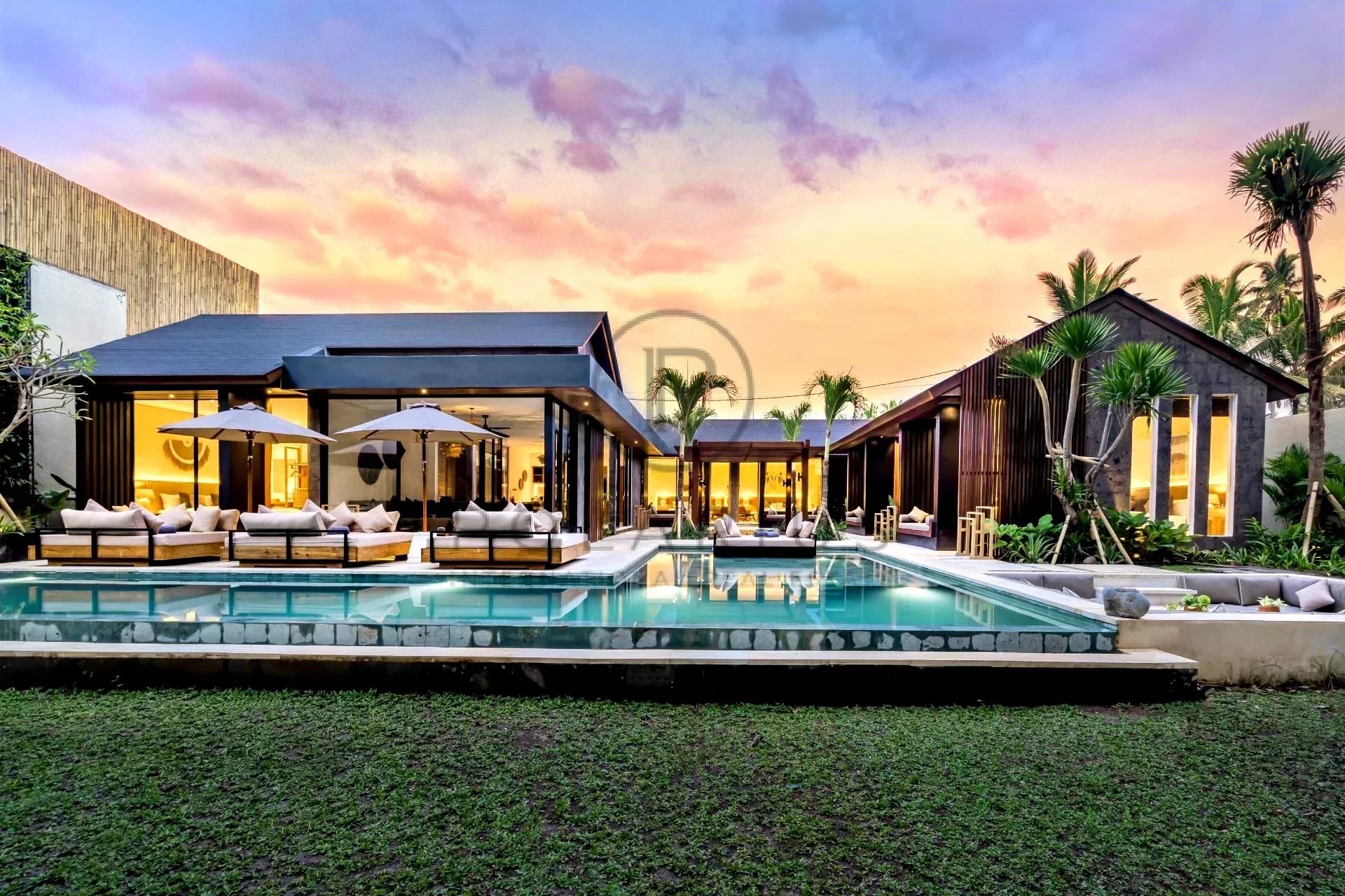 Villa moderne avec piscine, entourée de palmiers et baignée par un coucher de soleil coloré.