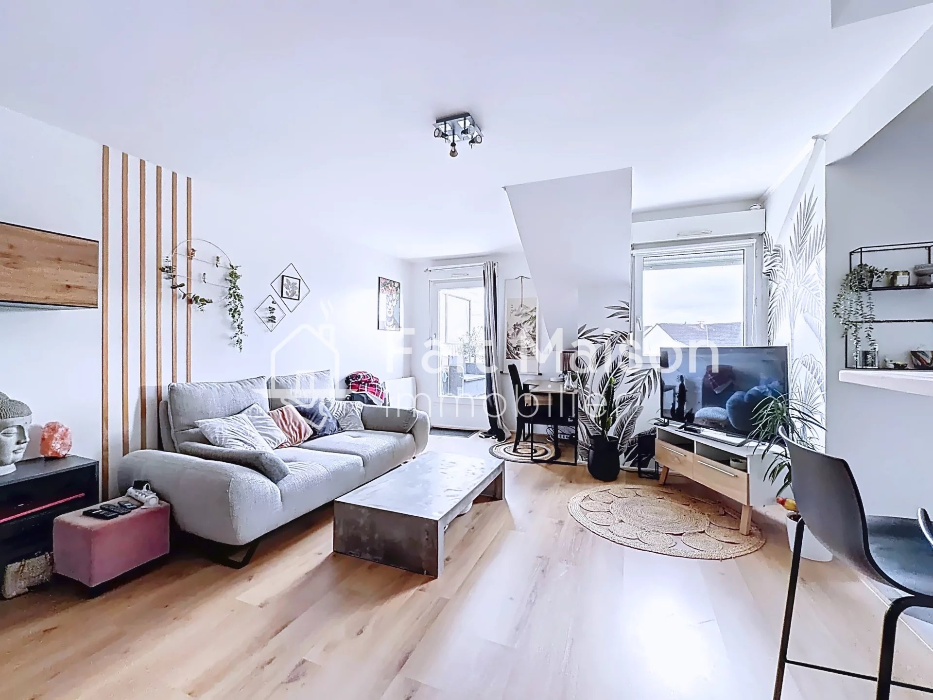 Un salon moderne avec un canapé, une télévision, et des plantes, décoré de manière épurée et lumineuse.