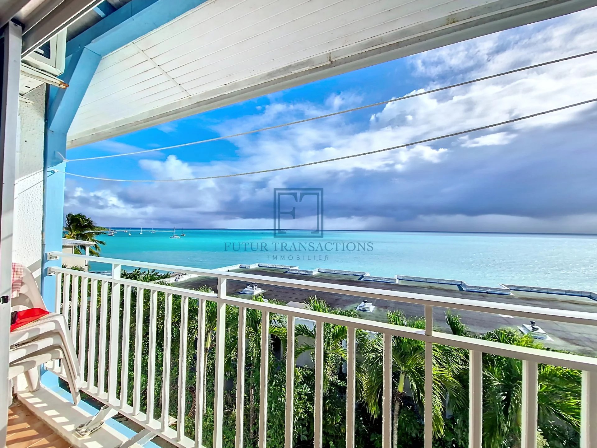 Vue sur la mer depuis un balcon, avec ciel bleu et eaux turquoise.