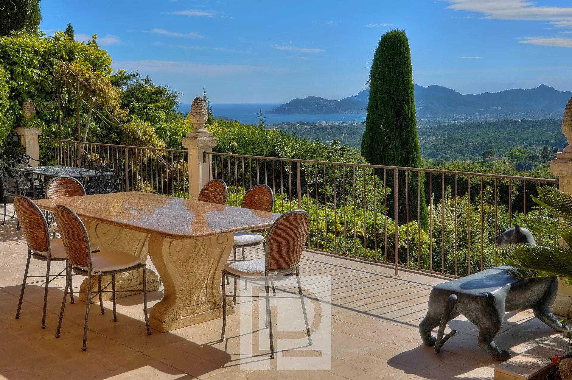 Terrasse ensoleillée avec table en pierre, offrant une vue panoramique sur les collines et la mer.