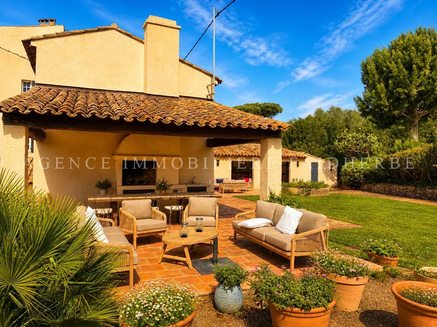 Belle terrasse ensoleillée avec mobilier confortable dans un jardin verdoyant.