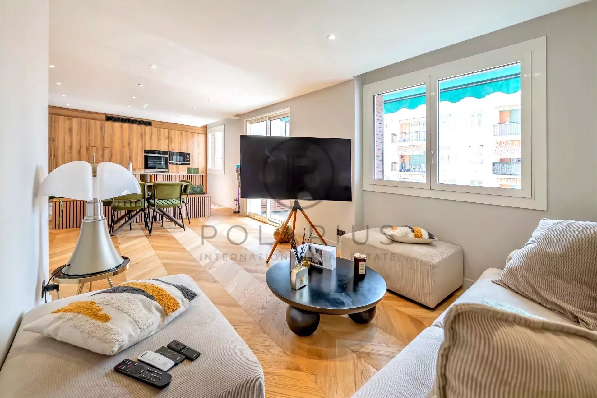 Helles, modernes Wohnzimmer mit Holzfußboden, gemütlichen Sofas, einem großen Fernseher und einem Esstisch im Hintergrund.