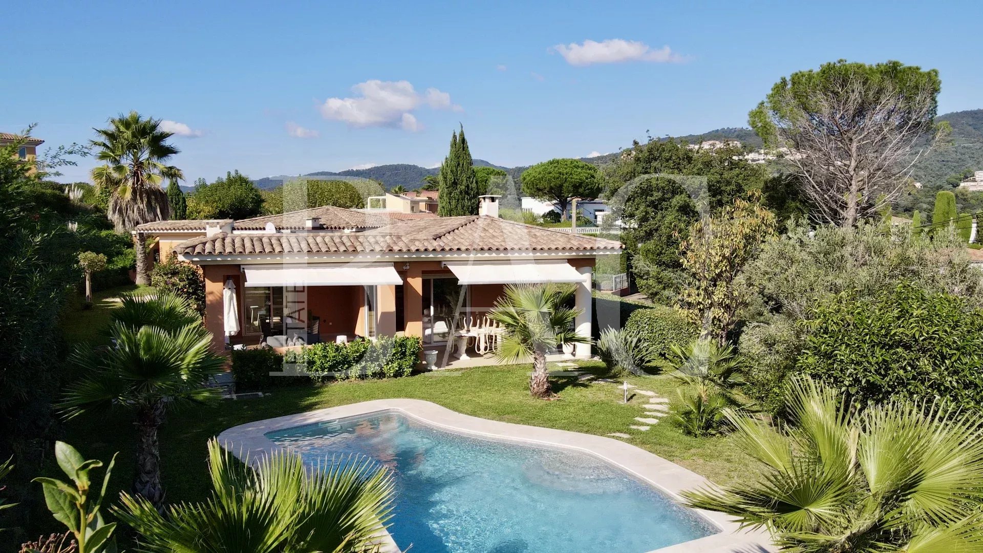 A cozy villa with a pool surrounded by lush greenery and palm trees under a clear blue sky.