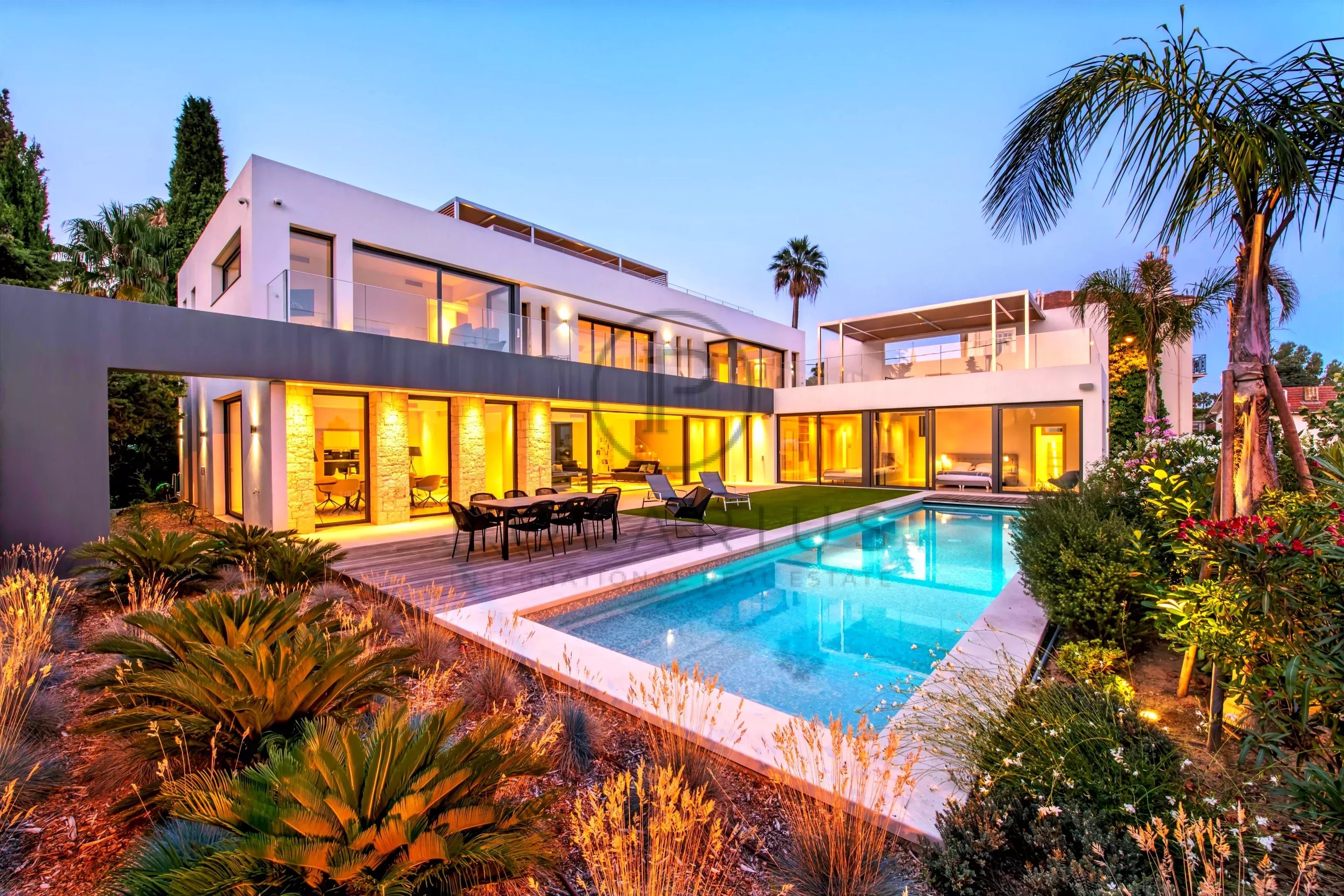 Une villa moderne avec piscine, entourée de jardins, éclairée au crépuscule.