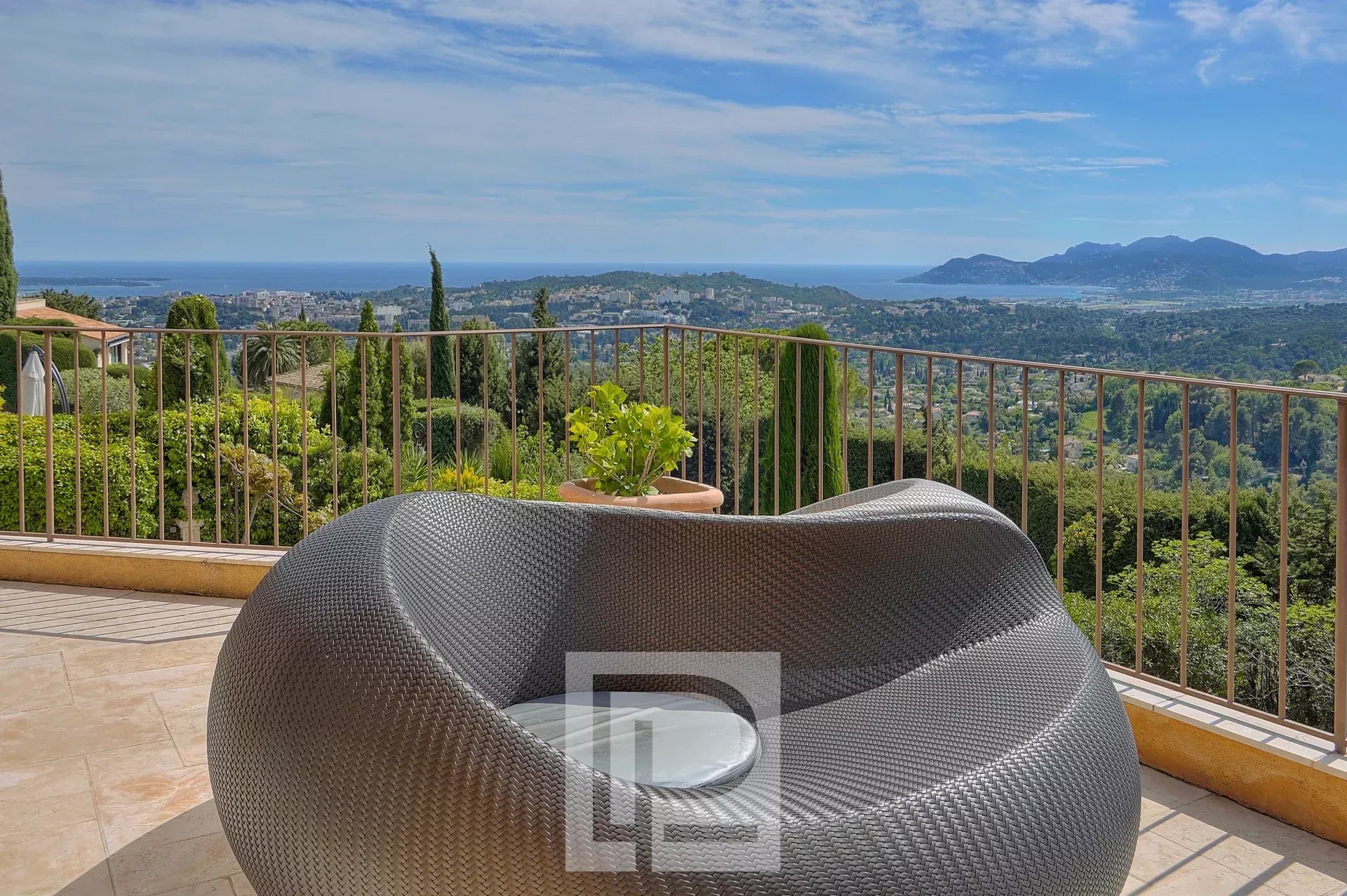 Une terrasse avec une chaise moderne offre une vue panoramique sur un paysage verdoyant et la mer au loin.