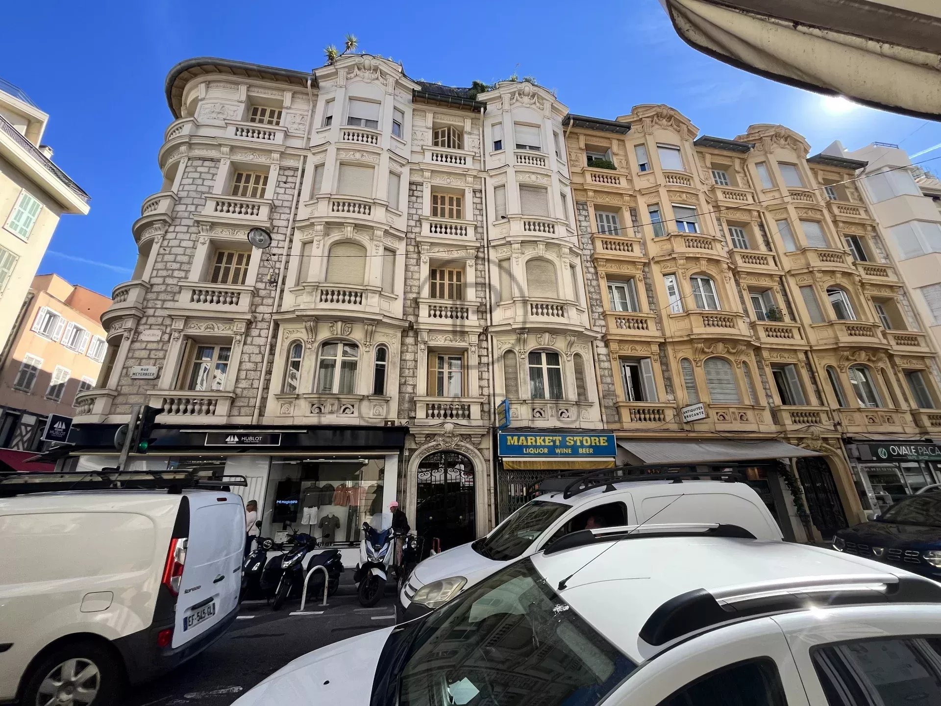 На фотографии изображены старинные здания с декоративными фасадами, расположенные на оживленной улице, припаркованы автомобили.