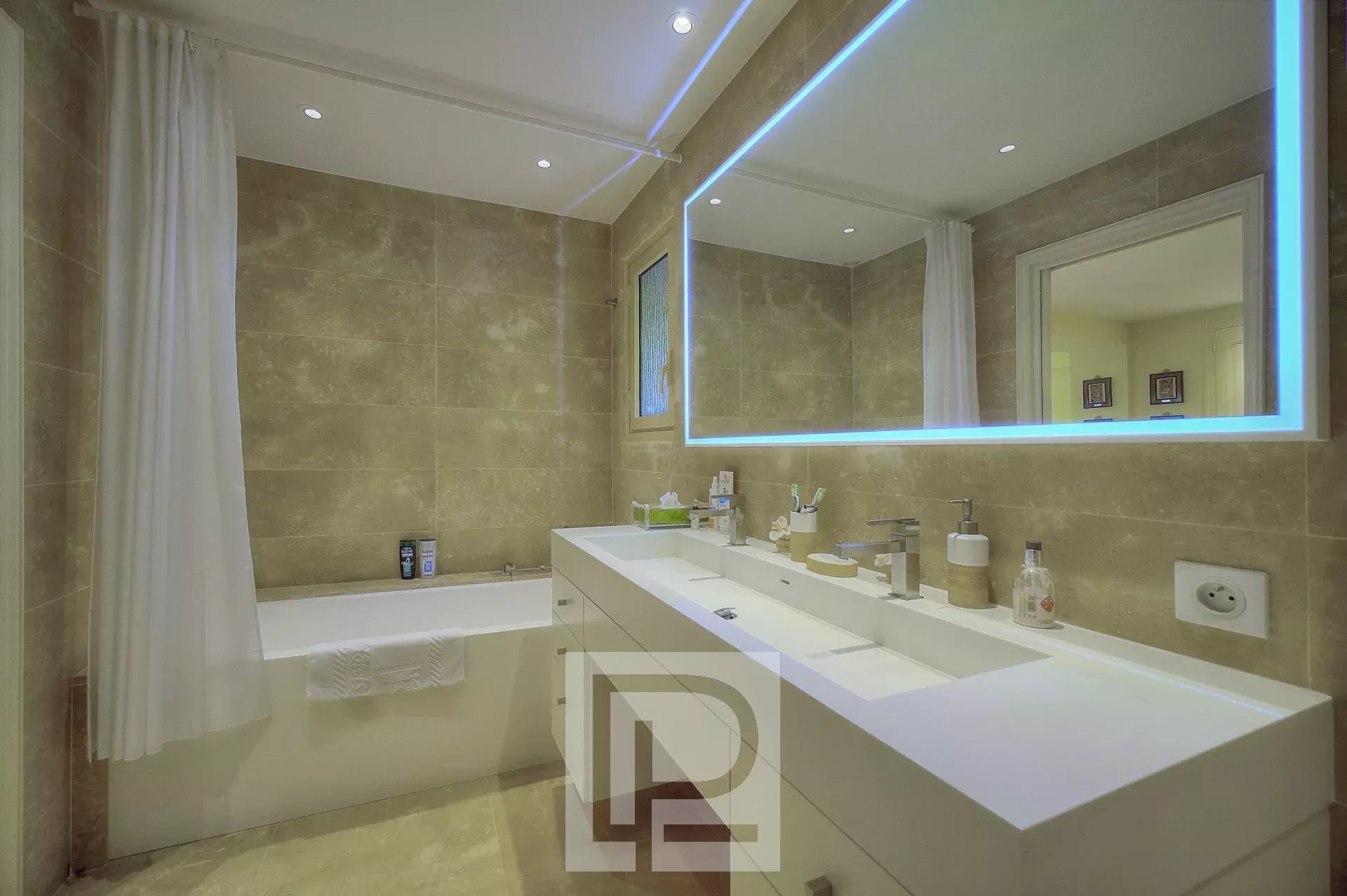 Salle de bain moderne avec baignoire, double vasque et miroir éclairé.