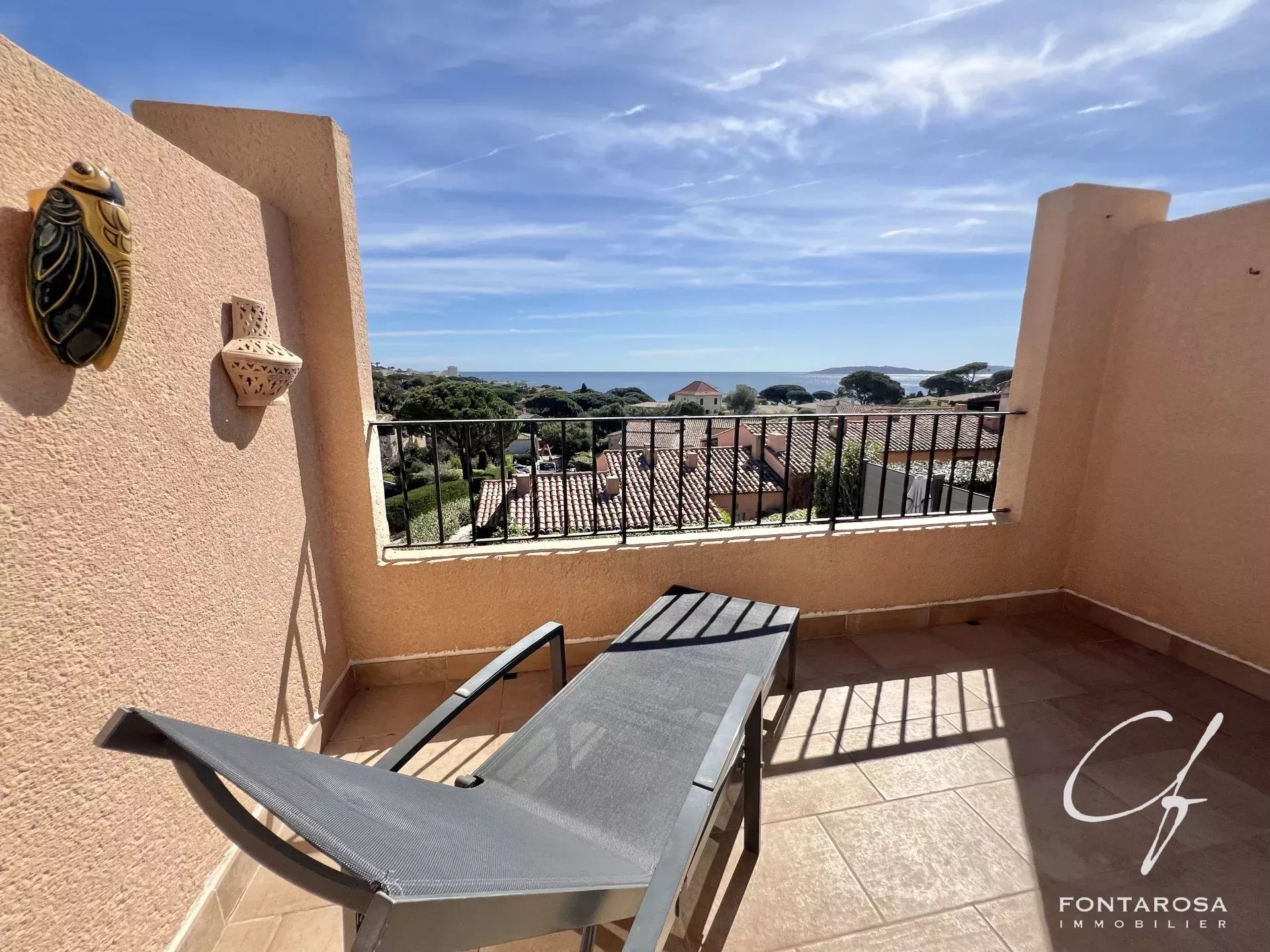 Une terrasse ensoleillée avec une chaise longue donnant sur la mer et les toits des maisons en contrebas.