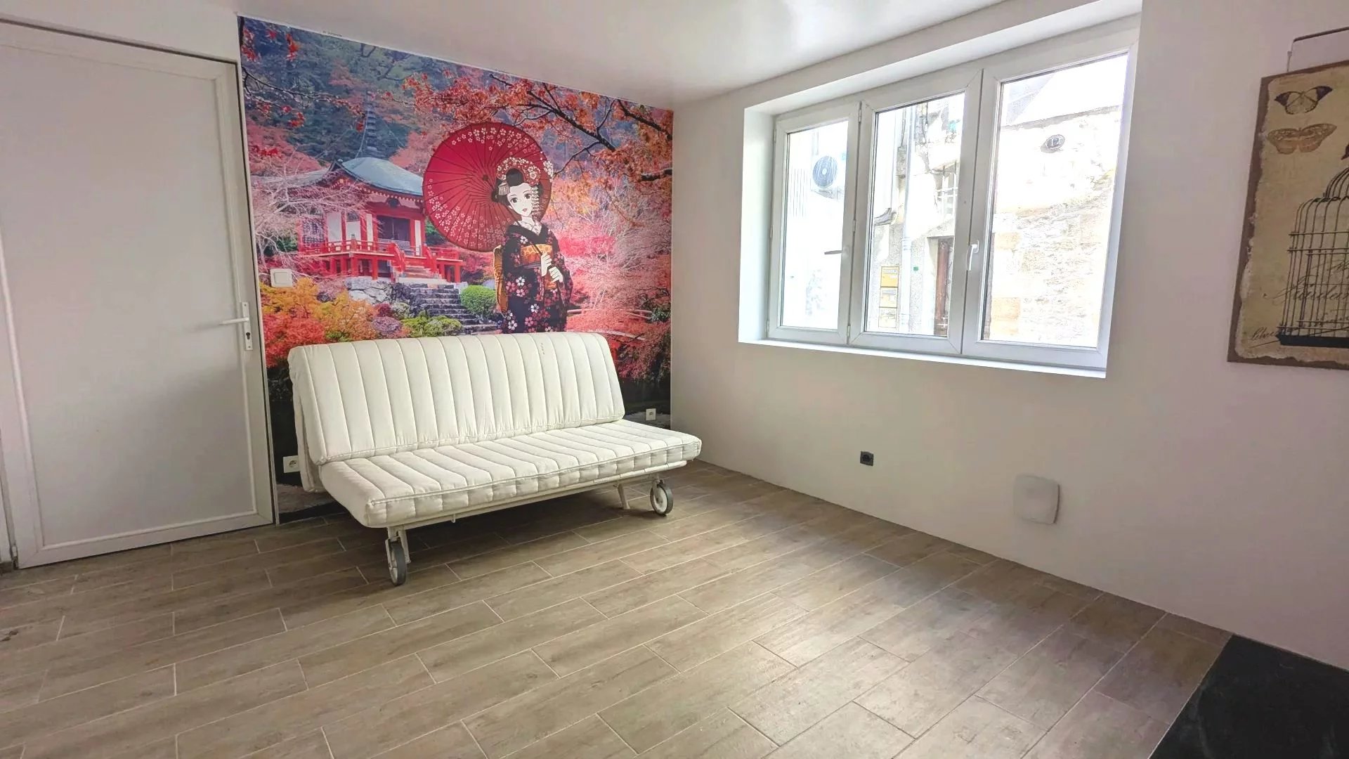 Un salon avec un canapé blanc, un mur décoré d'une fresque asiatique, et une grande fenêtre apportant de la lumière naturelle.