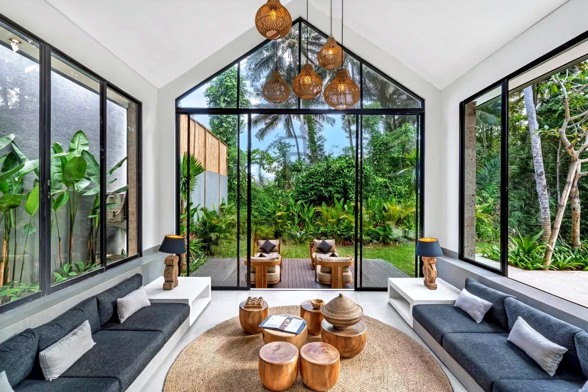 Ein moderner Raum mit großen Fenstern, gemütlichen Sofas und Holzmöbeln, der einen Blick auf einen grünen Garten bietet.