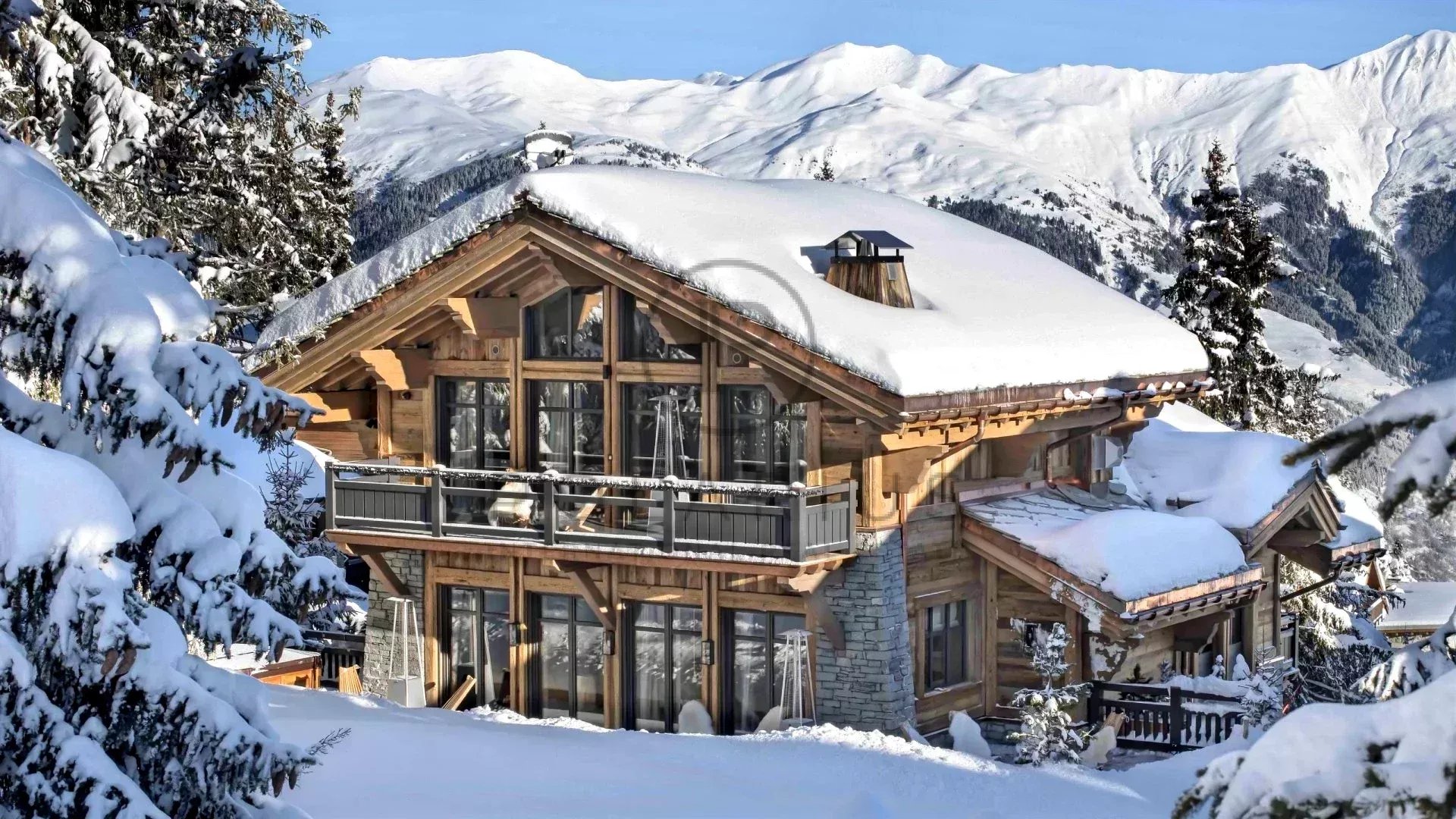 Chalet en bois entouré de neige avec des montagnes en arrière-plan.