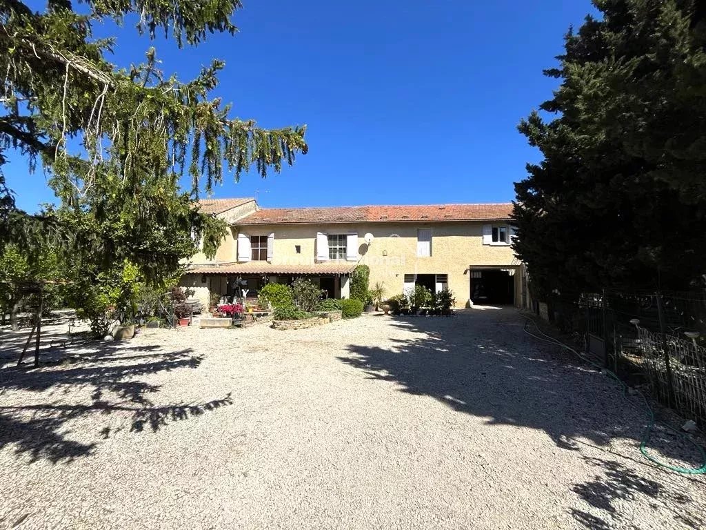 PERNES LES FONTAINES - Grande maison en pierre avec un jardin et des arbres sous un ciel bleu clair.