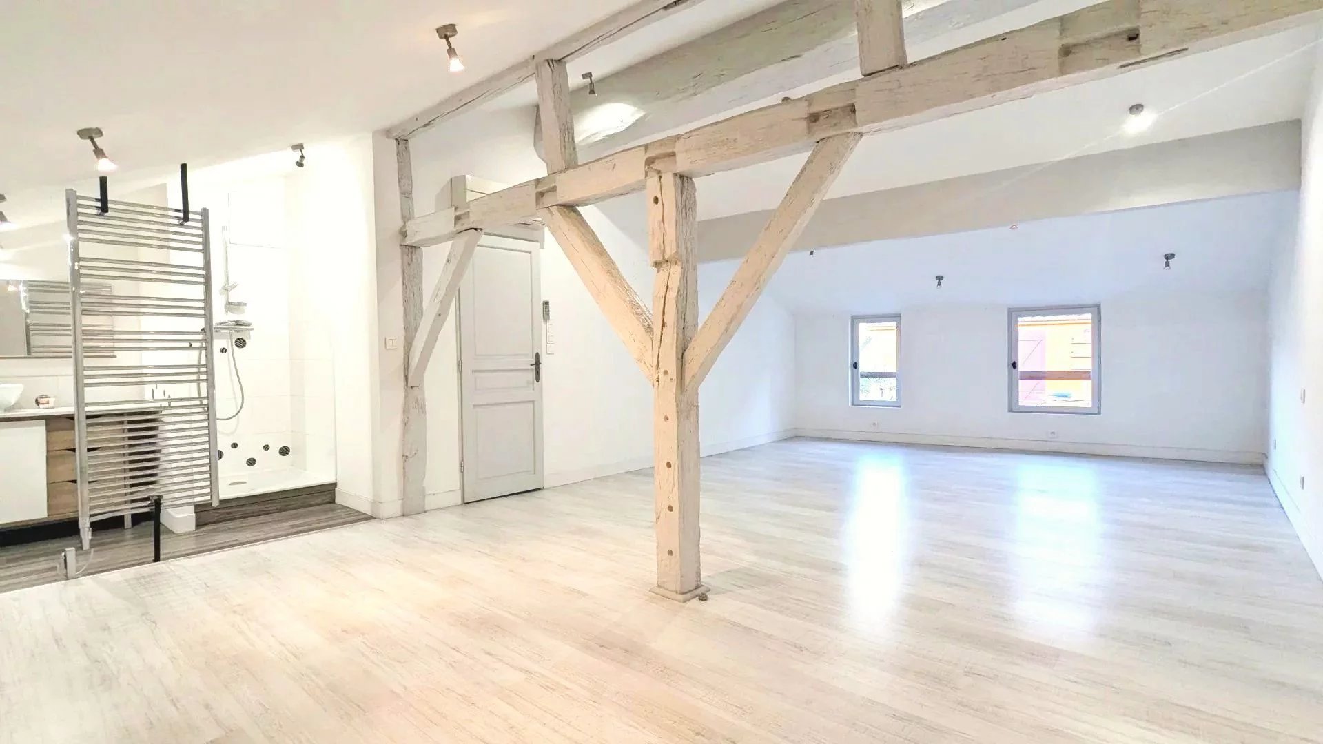 Un grand loft lumineux avec des poutres apparentes et un sol en bois clair.