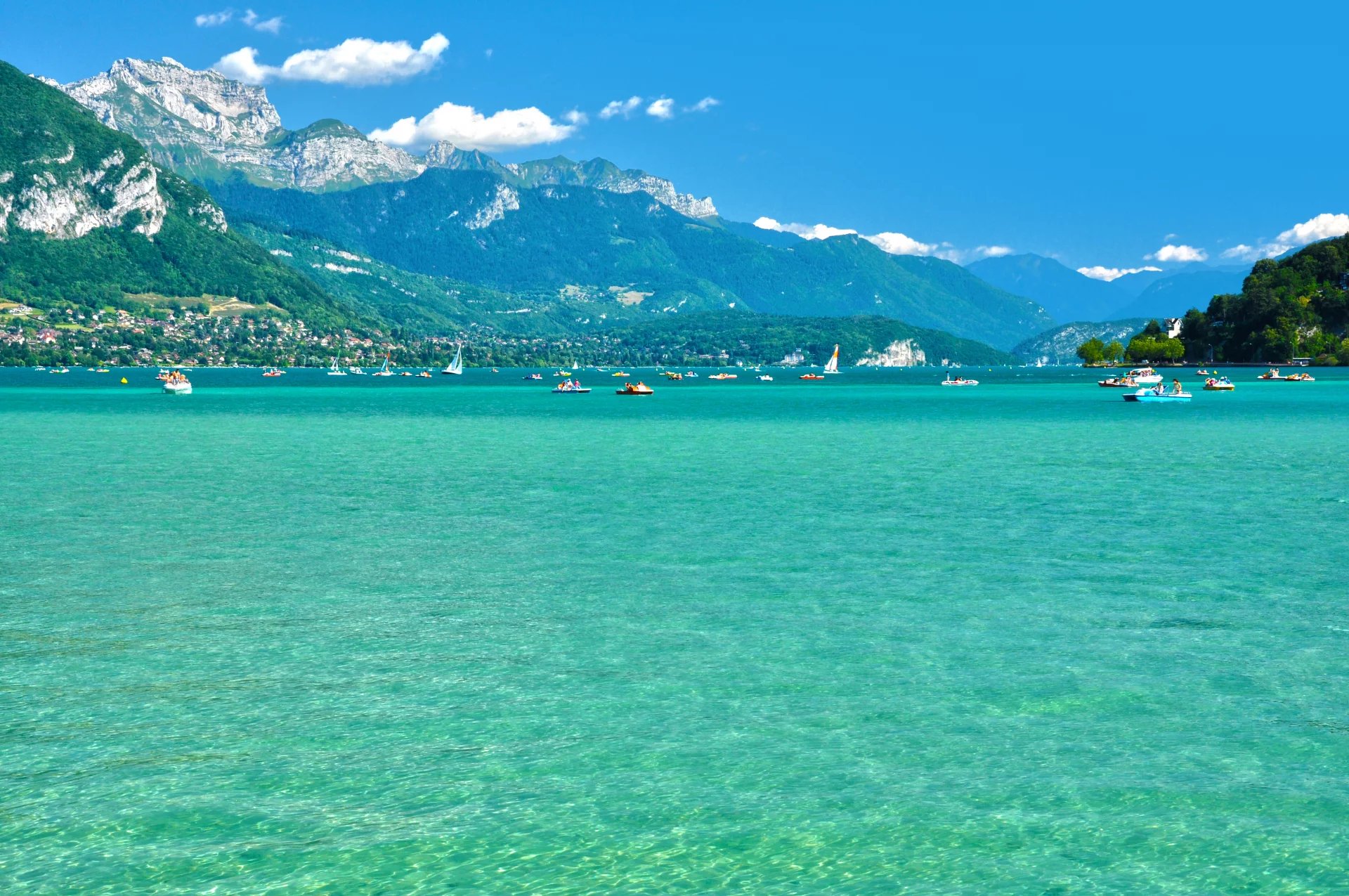 Lac d' ANNECY aux eaux turquoise entouré de montagnes verdoyantes sous un ciel bleu.