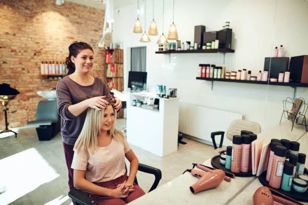 Young blonde woman smiling and looking at her reflection in a mirror while sitting in a salon chair during an appointment with her hairstylist